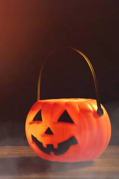 istock Halloween concept - Orange plastic pumpkin lantern on a dark wooden table with blurry sparkling light in the background, trick or treat. 1167558586