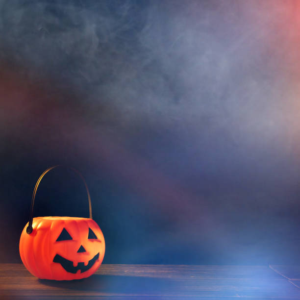 istock Halloween concept - Orange plastic pumpkin lantern on a dark wooden table with blurry sparkling light in the background, trick or treat. 1167558664