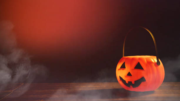 istock Halloween concept - Orange plastic pumpkin lantern on a dark wooden table with blurry sparkling light in the background, trick or treat. 1167558667