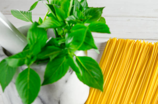 Leaves of green basil in a marble mortar and paste on a white wooden table