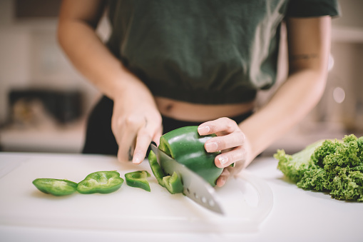 an asian chinese female preparing vegan food at kitchen counter cutting green pepper on chopping board