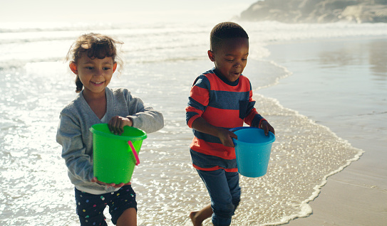 Cropped shot of two young children carrying buckets filled with water before building sandcastles on the beach