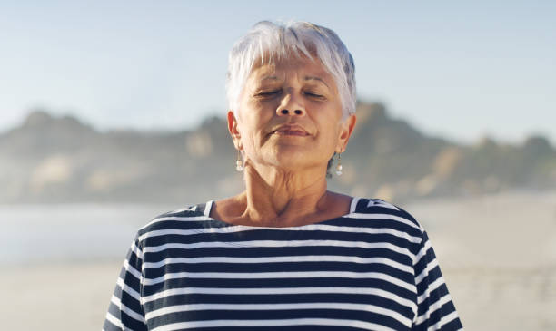 The fresh air is just what I needed Cropped shot of an attractive senior woman taking a deep breath while standing alone on the beach inhaling stock pictures, royalty-free photos & images