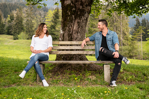 Pregnant woman resting in the mountains with her husband. They are looking at each other and wear fancy jeans.
