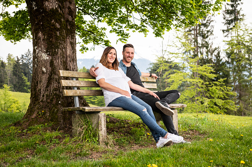 Pregnant woman resting in the mountains with her husband. They are holding hands and wear fancy jeans.