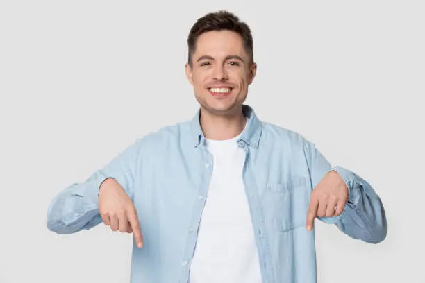 Photo of Happy man isolated on grey background pointing fingers down