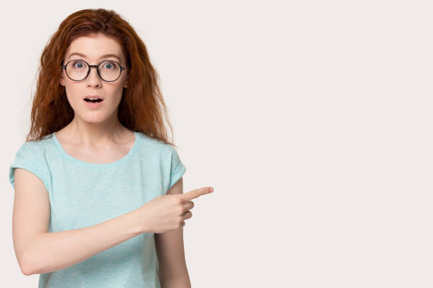 istock Red-headed female feels astonished point finger aside on copyspace 1167561261