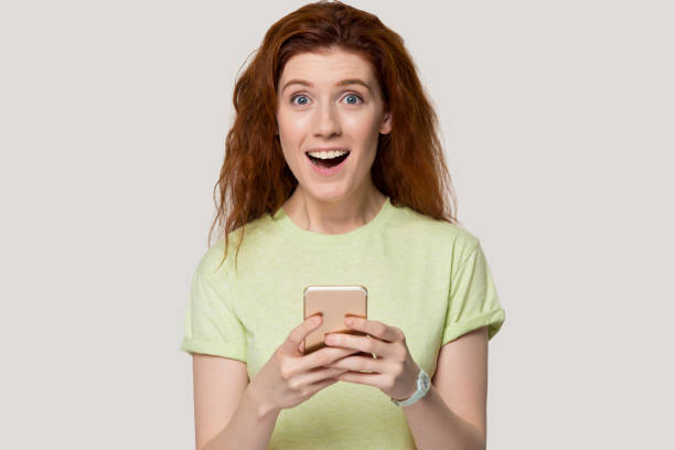istock Redhead surprised woman hold smartphone looking at camera studio shot 1167561639