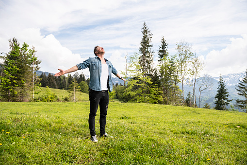 Handsome man is standing in the mountains with his arms wide open. Concept: back to nature, simple life