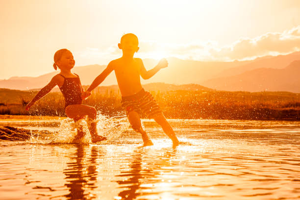 Pre-teen girl and boy sitting on sandy beach by the river. Shooting at morning while walking at sunny summer day