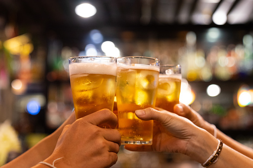 Group of happy friends drinking and toasting beer at brewery bar restaurant - Friendship concept with young people having fun together at cool vintage pub - Focus on middle pint glass