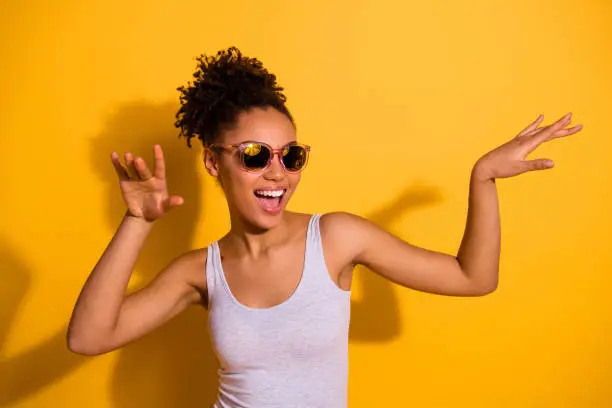 Close up photo beautiful nice pretty she her dark skin lady summer, weekend rest relax dancing festive vacation fest modern moves motion wear sun specs casual tank-top isolated bright yellow background