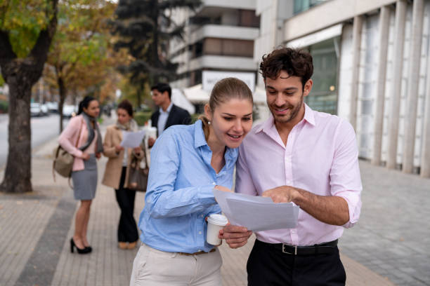 istock Cheerful business couple checking a document while drinking a coffee to go - Incidental people at background 1167579789