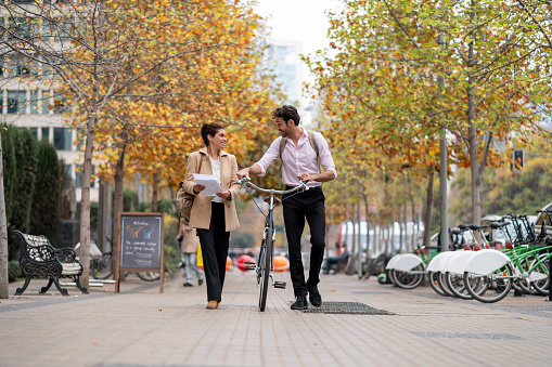 Cheerful business couple walking to the office and man taking his bicycle both smiling very happy