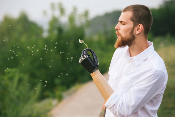 Young Man With Artificial limb is holding dandelion and blowing on it stock photo