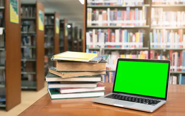 Photo of Computer laptop with green screen and book stack in library room.education background concept