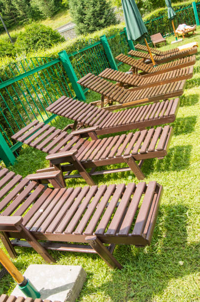 drewniane leżaki wystukają zieloną trawę pod słońcem w strefie relaksacyjnej nowoczesnego luksusowego hotelu. ogród do opalania i relaksu, fotografii pionowej - tanning bed brown relaxation resting zdjęcia i obrazy z banku zdjęć