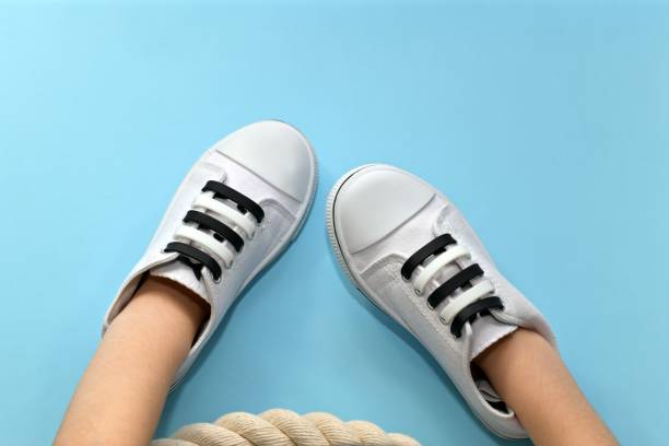 Sports shoes worn on hands. White athletic shoes, with silicone black and white laced stripes alternating in color. Put on children hands. In a marine style with a rope on a blue background below. lace fastener photos stock pictures, royalty-free photos & images