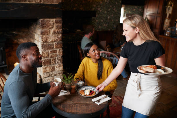 Waitress Working In Traditional English Pub Serving Breakfast To Guests Waitress Working In Traditional English Pub Serving Breakfast To Guests serving food and drinks photos stock pictures, royalty-free photos & images