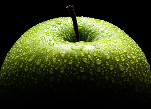 Green apple closeup macro on black ground and water drops