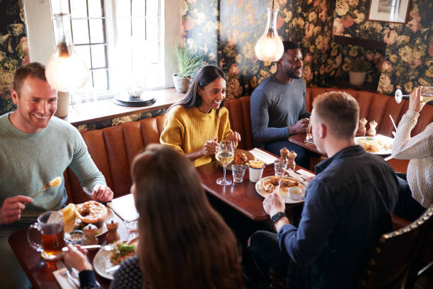 Group Of People Eating In Restaurant Of Busy Traditional English Pub Group Of People Eating In Restaurant Of Busy Traditional English Pub english spoken stock pictures, royalty-free photos & images