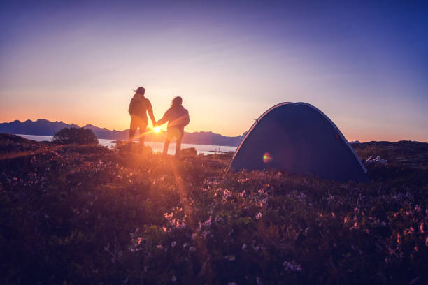 手をつないでテントの近くで夕日を眺め、ノルウェー、ロフォーテン諸島を探索する旅行キャンプアドベンチャーを見ているカップル - lofoten scandinavian norway nature ストックフォトと画像