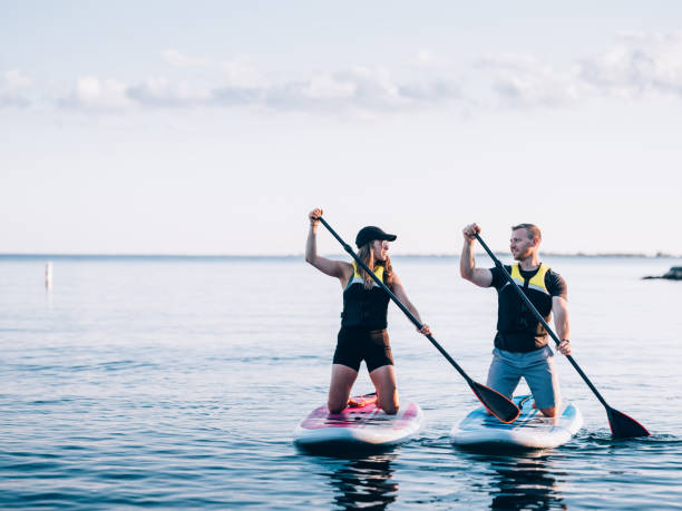 On the Lake Millennial couple Paddle boarding on Lake Ontario in the evening. paddleboard stock pictures, royalty-free photos & images