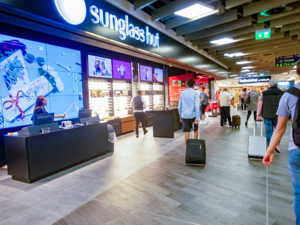 Departure lounge Luton Airport Luton, UK. Departure lounge at Luton Airport with travellers walking past stores across the tiled floor towards departure gates. sunglass hut stock pictures, royalty-free photos & images
