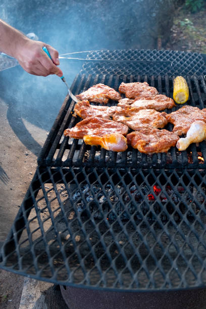 mann kochen essen, gegrilltes fleisch. die hände des menschen drehen fleischstücke auf einem metallrost um. ein grill auf offenem feuer. vertikale senkrechtes foto. - rotisserie chicken oven barbecue stock-fotos und bilder