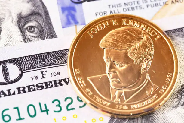 macro one dollar golden coin with John F. Kennedy portrait, and hundred dollars banknotes