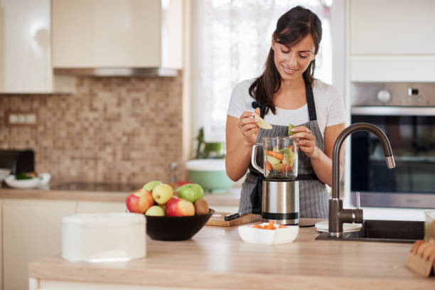istock Woman putting vegetables and fruits in blender while standing in kitchen. 1167641004