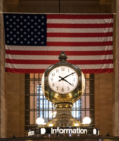 The clock in the main concourse of Grand Central Terminal, New York City. US flag in ba ckground. background.