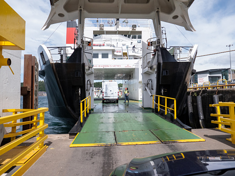 12th June 2019: Driving onto a passenger roll on roll off, RORO, ferry at Oban harbour on the northwest coast of Scotland. The stern of the hull is raised open and a ramp lowered for vehicles and foot passengers to board. On arrival at their destination the bow of the hull opens to let vehicles drive straight out. A crew worker is standing on the ferry deck to guide drivers on where to park, before being asked to go up to an upper deck for the duration of the crossing.