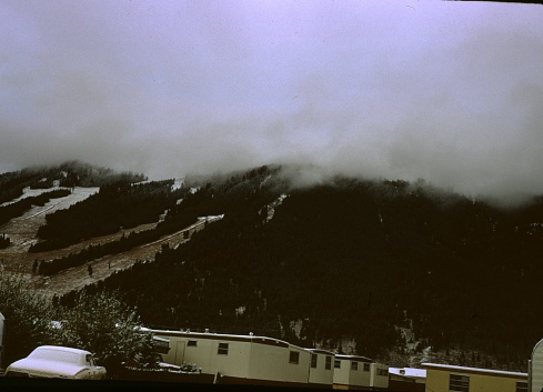 United States - January 01, 1970:  Snowy mountainous wooded area with snow-covered mobile homes and a car in a trailer park, on a misty morning in Wyoming, 1970