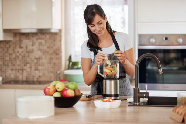 istock Woman putting vegetables and fruits in blender while standing in kitchen. 1167641985