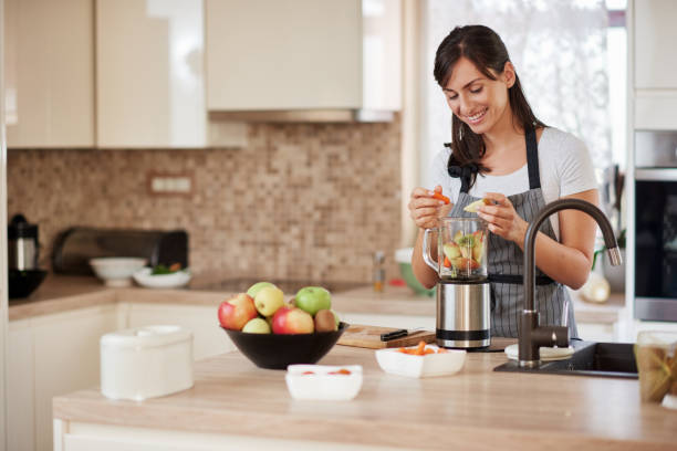 istock Woman putting vegetables and fruits in blender while standing in kitchen. 1167642649