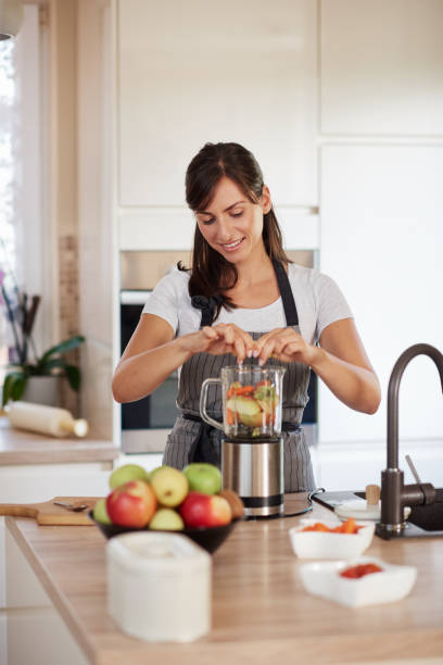 istock Woman putting vegetables and fruits in blender while standing in kitchen. 1167642700
