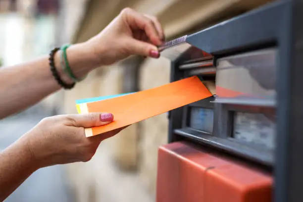 Woman inserting envelope into public mailbox at post office. Female hand sending letter