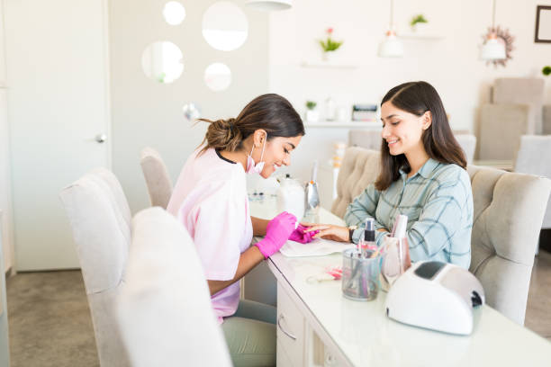 Closeup Of Beautician Applying Nail At Salon Smiling manicurist decorating nails with color on client's hand at beauty spa manicure stock pictures, royalty-free photos & images