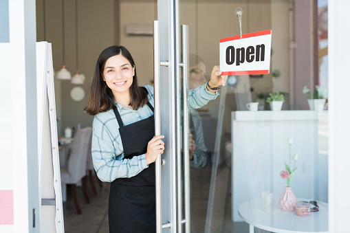 Smiling confident Latin owner turning open sign on glass door of spa