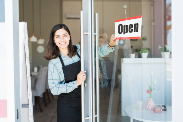 We Are Ready To Serve You At Salon Smiling confident Latin owner turning open sign on glass door of spa hello stock pictures, royalty-free photos & images