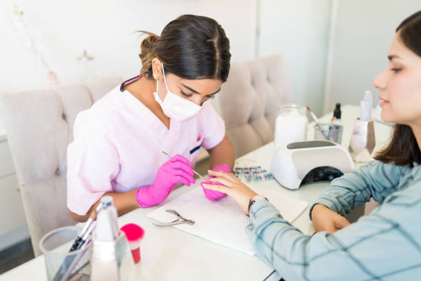 Receiving Manicure Treatment In Beauty Salon High angle view of young beautician giving manicure to female customer at nail salon cuticle photos stock pictures, royalty-free photos & images