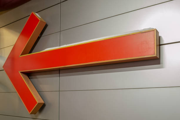 istock Large arrow-shaped pointer. Orange. Hanging on a gray steel wall. 1167664893