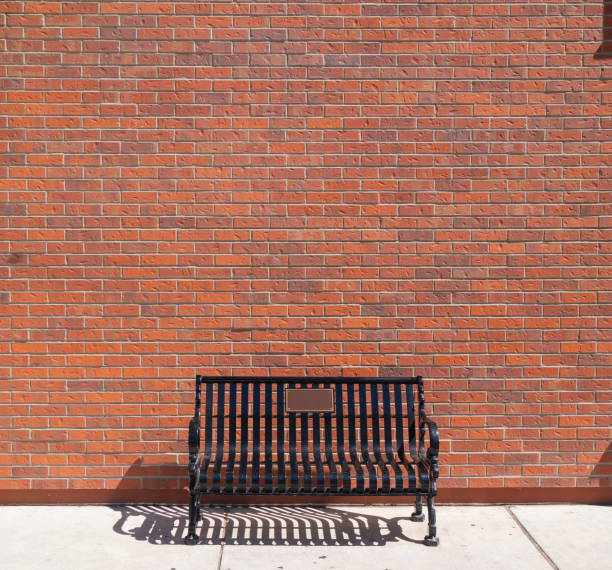 An empty bench sits in front of black brick wall.