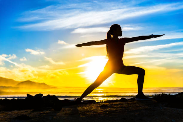 Fitness silhouette practicing warrior II yoga pose Silhouette of fitness athlete practicing warrior II yoga pose meditating at beach sunset. Woman stretching doing morning meditation against colorful sky background. Zen wellness and wellbeing concept. warrior position stock pictures, royalty-free photos & images