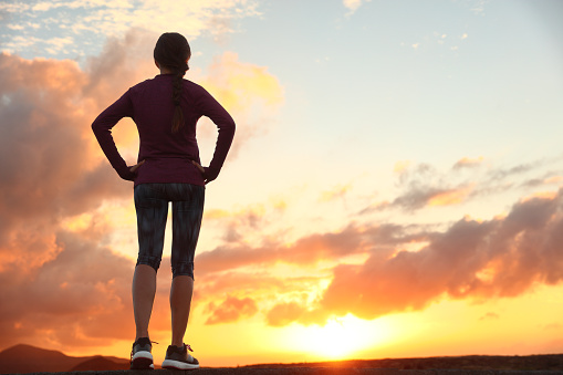 Active woman looking ahead at sunset sky for life challenge. Runner athlete getting ready for trail run thinking goal achievement choice and happiness. Female sports person living healthy lifestyle.