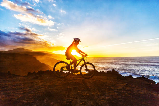 Mountain Biking Cyclist Woman Bike Trail Cycling Mountain biking MTB cyclist woman cycling on bike trail on coast at sunset. Person on bike by sea in sportswear with bicycle enjoying healthy active lifestyle in beautiful nature. female mountain biker silhouette stock pictures, royalty-free photos & images