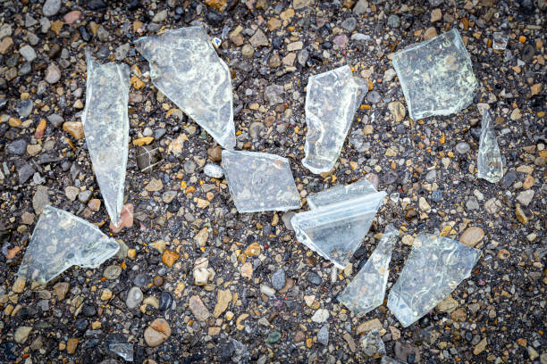 horizontal close up image of broken and shattered sharp pieces glass lying on a pebbled walkway.