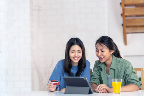 candid of young attractive asian two girls sitting at home holding discount credit card in hand paying for shopping online at tablet smartphone in omni channel concept. asian youth casual lifestyle. - laptop women child digital tablet imagens e fotografias de stock