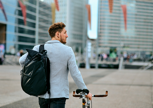 Rearview shot of a young businessman traveling through the city with his bicycle